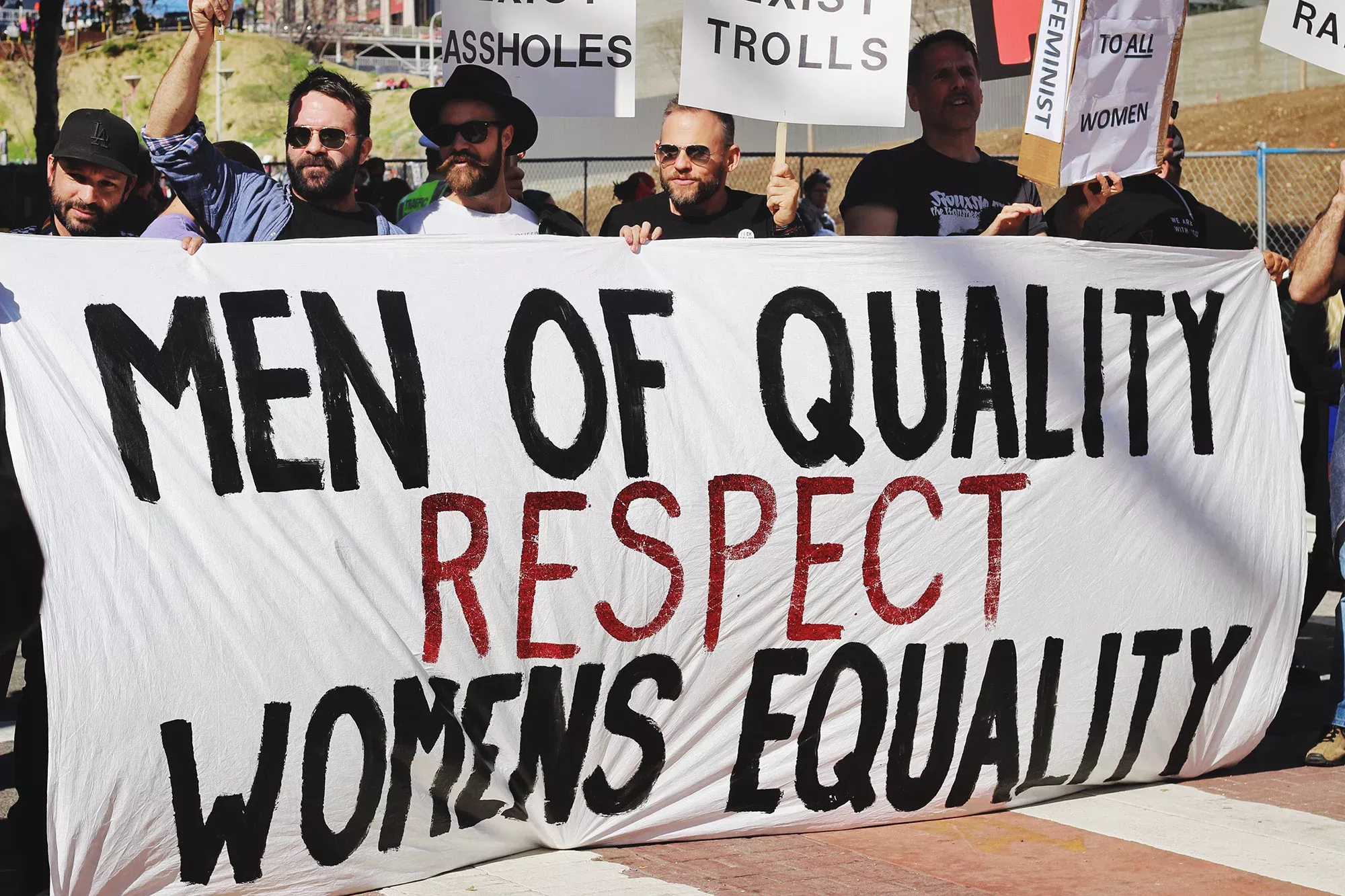 Männer auf einer Demo, Banner mit Text "Men of quality respect womens equality", Gefühl von Gemeinschaft und Solidarität