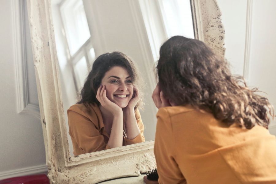 Frau lächelt sich selbst im Spiegel an, Gefühl von Freude, Selbstliebe
