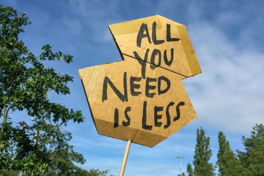 Pappschild, weiter Hintergrund, blauer Himmel, "all you need is less", Gefühl von Achtsamkeit