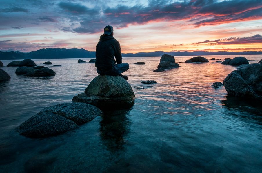 Person sitzt auf einen Stein im Meer beim Sonnenuntergang, Gefühl von Weite, Nachdenklichkeit, Ruhe