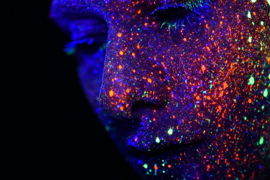 Nahaufnahme Gesicht, gespränkelt mit fluoreszierende farbe in Schwarzlicht, Gefühl von Vielfalt