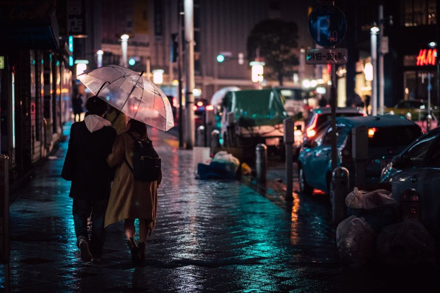 Zwei Personen unter einem Regenschirm am Abend in einer leicht erleuchteten Innenstadt, Gefühl von Gemeinschaft, Vertrauen